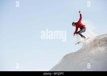 Foto von Mann in Helm mit Snowboard springen von Verschneiten Berghang Stockfoto