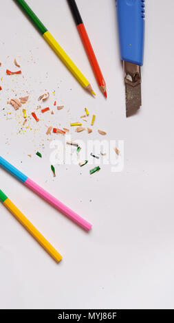 Flach der Buntstifte und eine blaue Cuttermesser mit bunten Pencil shavings verstreut herum, auf weissem Papier Hintergrund. Stockfoto