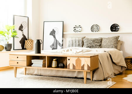 Afrikanische Poster neben Bett mit gemusterten Kissen im Schlafzimmer Innenraum mit holzschrank Stockfoto