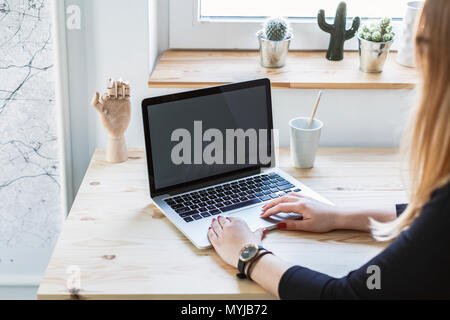 Frau Tippen auf Laptop mit Mockup vom Schreibtisch aus Holz im Home Office Interior Stockfoto