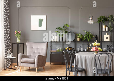 Beige Sessel gegen graue Wand mit Poster im Innenbereich mit Stühlen am Tisch. Real Photo Stockfoto
