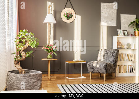 Bonsai Baum in einem Stoff Topf Deckel, Tulpen auf einem Holztisch, Bücherregal und gemusterte Sessel im Wohnzimmer Innenraum Stockfoto