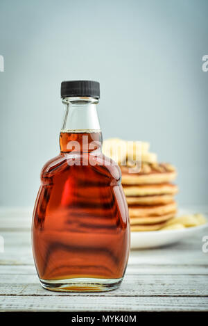 Ahornsirup in Glasflasche mit Pfannkuchen auf hölzernen Hintergrund Stockfoto
