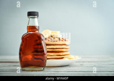 Ahornsirup in Glasflasche mit Pfannkuchen auf hölzernen Hintergrund Stockfoto