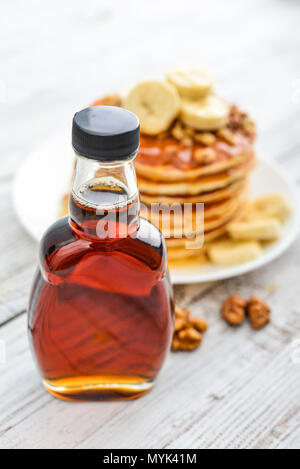 Ahornsirup in Glasflasche mit Pfannkuchen auf hölzernen Hintergrund Stockfoto