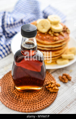 Ahornsirup in Glasflasche mit Pfannkuchen auf hölzernen Hintergrund Stockfoto
