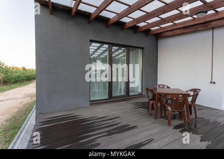 Seitenansicht eines offenen Veranda vor einem modernen Forest Cottage. Kiefer junge Wald unter den Sonnenuntergang strahlen im Hintergrund. Stockfoto