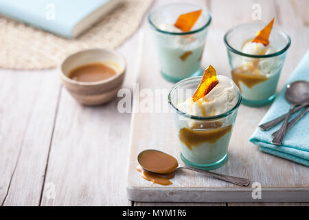 Vanille Eis im Glas serviert Gerichte mit Butterscotch Sauce und Karamell shard auf einem urigen weiß Arbeitsplatte aus Holz Stockfoto