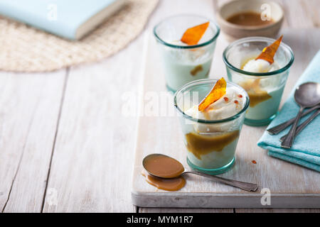 Vanille Eis im Glas serviert Gerichte mit Butterscotch Sauce und Karamell shard auf einem urigen weiß Arbeitsplatte aus Holz Stockfoto