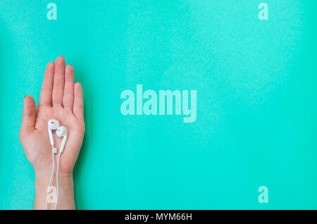 Lady's Hand mit schönen Maniküre holding Ohrhörer auf Türkis Farbe Hintergrund. Stockfoto