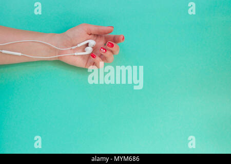 Lady's Hand mit schönen Maniküre holding Ohrhörer auf Türkis Farbe Hintergrund. Stockfoto