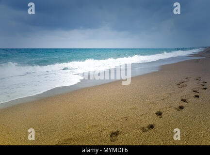 Linie der Fußspuren im Sand an einem einsamen Strand von der Kamera entfernt am Rande des Surf mit einem ruhigen Meer führenden Stockfoto