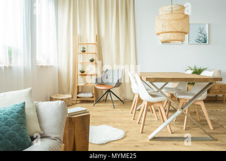 Rattan Lampe über Tisch und Stühle in der multifunktionalen Esszimmer mit Sofa und Poster an der Wand Stockfoto