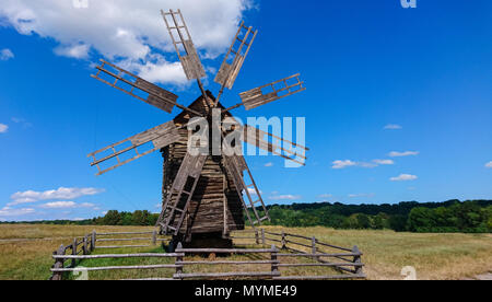 Alte historische Windmühle aus Holz mit gebrochenen verfallenen Segel umzäunten in einem offenen Feld auf einem sonnigen blauen Himmel Tag Stockfoto