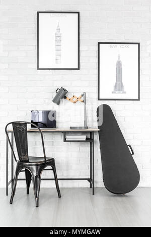 Schwarze E-Gitarre steht neben einem hölzernen Schreibtisch mit Laptop und handgefertigte Lampe im Zimmer mit Postern Stockfoto