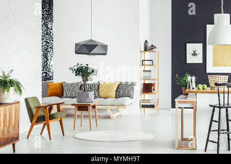 Kleiner Baum im Topf auf Material Holz Tisch neben Vintage grün Stuhl im Zimmer mit gemusterten Kissen auf dem Sofa Stockfoto