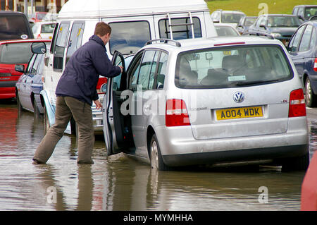 Flutung in Southend am Meer. Der Mann wasiert durch Wasser zu seinem Auto. Die Frühjahrsflut brach gegen die Verteidigung des Meeres Stockfoto