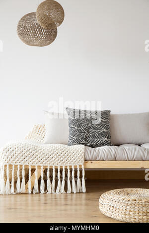 Gemusterte Decke auf Bett aus Holz, Puff und Lampen in helles Schlafzimmer mit Kopie Speicherplatz auf der weißen Wand Stockfoto