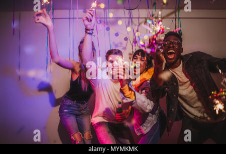 Freunde feiern und Spielen mit Feuer glitzert an einem Haus Party. Junge Männer und Frauen, die Spaß an einem bunten House Party mit Dekorationen und con Stockfoto