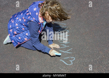 Das Kind malt mit Kreide auf den Asphalt, ein kleines Mädchen in windigen Wetter verschiedenen Beschriftungen schreibt Stockfoto