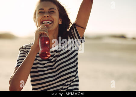 Fröhliche junge Frau, die im Freien und trinken Cola aus Glas Flasche. Frau genießen Sie erfrischende Getränk an einem heißen Sommertag. Stockfoto