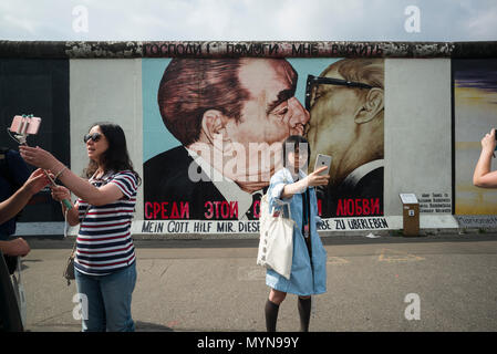 Berlin. Deutschland. Touristen posieren für Fotos vor einem der übrigen Abschnitte der Berliner Mauer an der East Side Gallery. Touristen posieren für ph Stockfoto