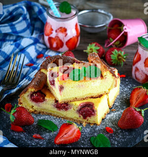 Stück Käsekuchen mit Erdbeeren auf schwarzem Graphit Platte, Ansicht von oben, neben frische reife Beeren Stockfoto