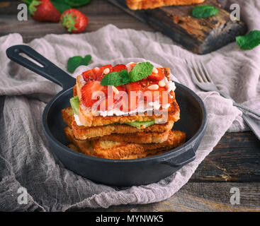 Stapel der French Toast von Weißbrot mit Hüttenkäse, Erdbeeren in einem schwarzen Gusseisernen runde Pfanne mit einem auf einem grauen Holztisch Griff Stockfoto