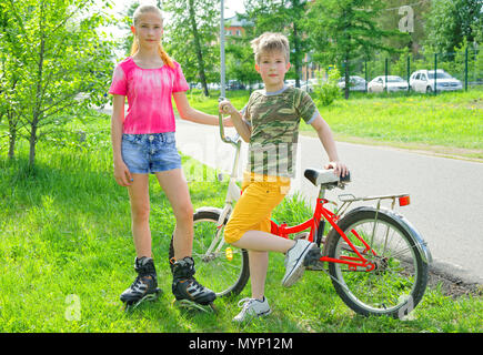 Heißer Sommer am Nachmittag. Aktiv Urlaub mit der ganzen Familie von Teenagern - Bruder und Schwester mit Rollschuhen und ein Fahrrad Stockfoto