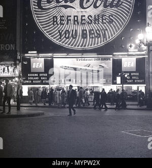 1960er Jahre, historisch, abends im Londoner West End und Leute am Piccadilly Circus in der Lower Regent Street außerhalb von Geschäften, mit den Neonwerbetafeln, die die Gegend beleuchten. Eine Werbetafel für die Trident-Flugzeuge von British European Airways (BEA) ist im Bild zu sehen. Stockfoto