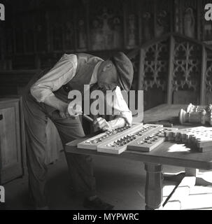 1950er Jahre, historische Bild zeigt einen älteren männlichen Handwerker oder woodworker in einem Workshop mit Hammer und Meißel zu Carve Out komplizierte Muster auf einem rechteckigen Stück Weichholz, England, UK. Stockfoto