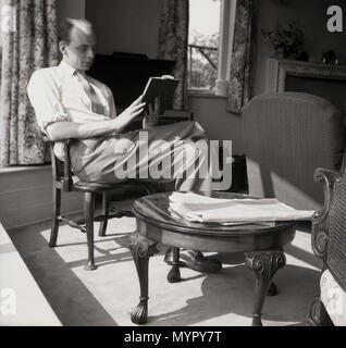 1953, Juli, ein erwachsener Mann, mit einem ungewöhnlichen Frisur, auf einem Stuhl sitzen in einem Zimmer vorne ein Buch lesen, England, UK. Stockfoto