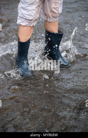 Jungen tragen Gummistiefel Spritzen in das Hochwasser in einer Straße nach schweren Regenfällen Stockfoto