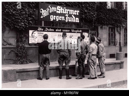 Die Nazi-Deutschland-Propagandazeitung Antisemitic der Stürmer aus dem Jahrgang 1930 erscheint auf der Straße mit NSDAP-Mitgliedern und einer bunten, aufgelösten Gruppe deutscher Männer, die die rassistisch-aufrührende Schlagzeile lesen, die lautet: „Die Juden sind unser Unglück“ Stadt Worms Nazi-Deutschland 1935 Stockfoto