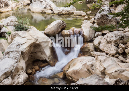 Ein ruhiger Wasserfall fällt durch glatte, verwitterte Felsen in einen ruhigen Wasserpool. Umgeben von üppigem Grün und natürlichen Felsformationen, Stockfoto