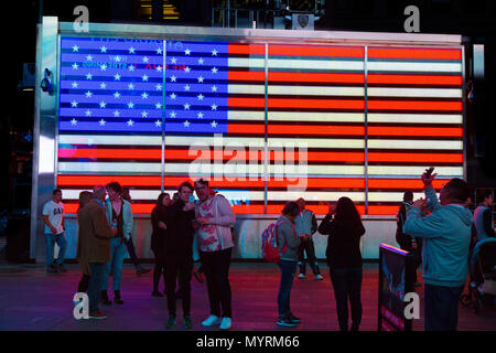 Touristen in Times Square vor einem großen Leuchtreklame der amerikanischen Flagge, New York City, USA Stockfoto