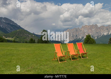 Orange und rote Liegestühle auf einer Wiese in den italienischen Alpen warten auf Menschen zu sitzen unten Stockfoto