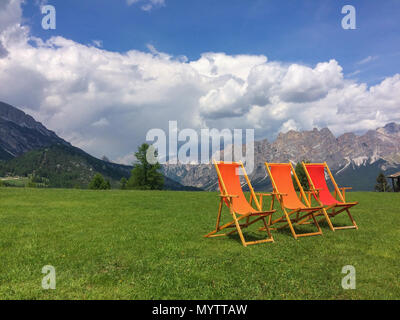Orange und rote Liegestühle auf einer Wiese in den italienischen Alpen warten auf Menschen zu sitzen unten Stockfoto