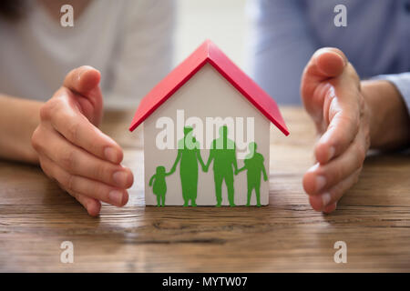 Die Paar schützende Hand Familie Papier Ausschneiden und Haus Modell über Holz- Schreibtisch Stockfoto