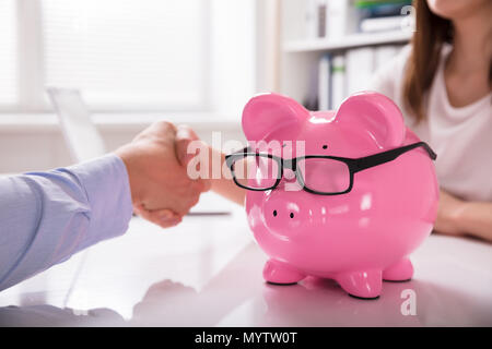 Zwei Geschäftspartnern zitternden Händen Neben rosa Sparschwein Stockfoto