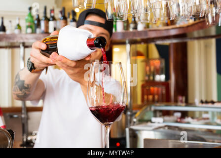 Barkeeper gießt aus einem Glas Rotwein an der Bar Stockfoto