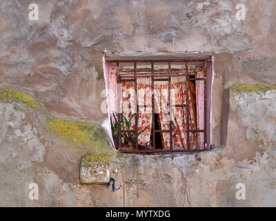 Fenster mit einem Vintage Metallgitter und pinkfarbenen Vorhängen auf der Peeling alte Mauer. Stockfoto