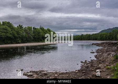 Torlundy, Schottland - Juni 11, 2012: Die grauen Fluss Lochy hinter Inverlochy Castle unter schweren dunklen Himmel. Bewaldete felsige Ufer. Fluss schützt die Ca Stockfoto