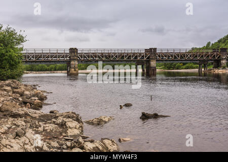 Torlundy, Schottland - Juni 11, 2012: Eisenbahnbrücke über den grauen Fluss Lochy hinter Inverlochy Castle unter schweren dunklen Himmel. Bewaldete felsige Ufer. Stockfoto