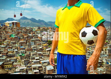 Brasilianische Fußballspieler im Vintage Style shirt Holding Fußball vor der Favela slum Hintergrund in Rio de Janeiro Stockfoto