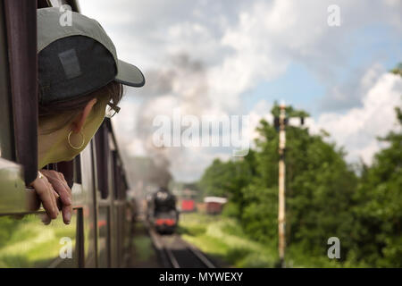 Rückansicht, weibliche Beifahrerin, die im Sommer mit dem alten britischen Dampfzug Severn Valley Railway den Kopf aus dem Fenster lehnt. Stockfoto
