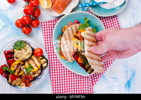 Tortilla mit Gemüse und Lachs in männlichen Händen. Fitness Nahrung. Gesundes Mittagessen. .. Stockfoto