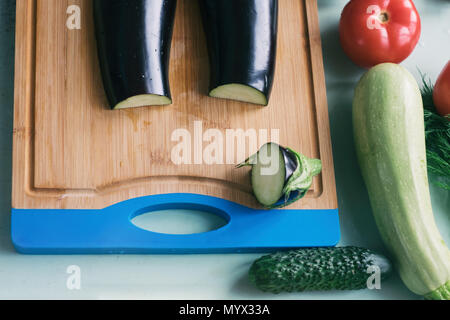Layout der ganze und aufgeschnittene Auberginen, Schneidbrett und anderen frischen Gemüse. Stockfoto