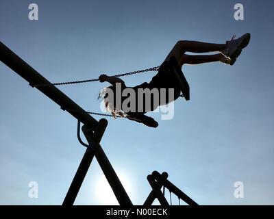 UK-Wetter: sonnig Abend in Adlington, Lancashire. Junges Mädchen abkühlen nach einem heißen Tag durch Schwingen gegen den strahlend blauen Abendhimmel. Stockfoto