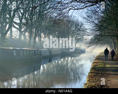 Wetter in Großbritannien: Sonnig und frostig in Adlington. Reflexionen von schmalen Booten und Bäumen auf dem Leeds- und Liverpool-Kanal bei Adlington in Lancashire mit zwei Personen, die auf einem Schleppweg laufen Stockfoto